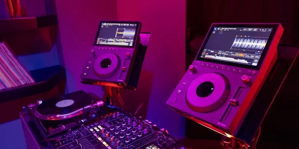 Cabina con dos AlphaTheta CDJ-1500X, un mixer DJ y una tornamesa bajo luces de club