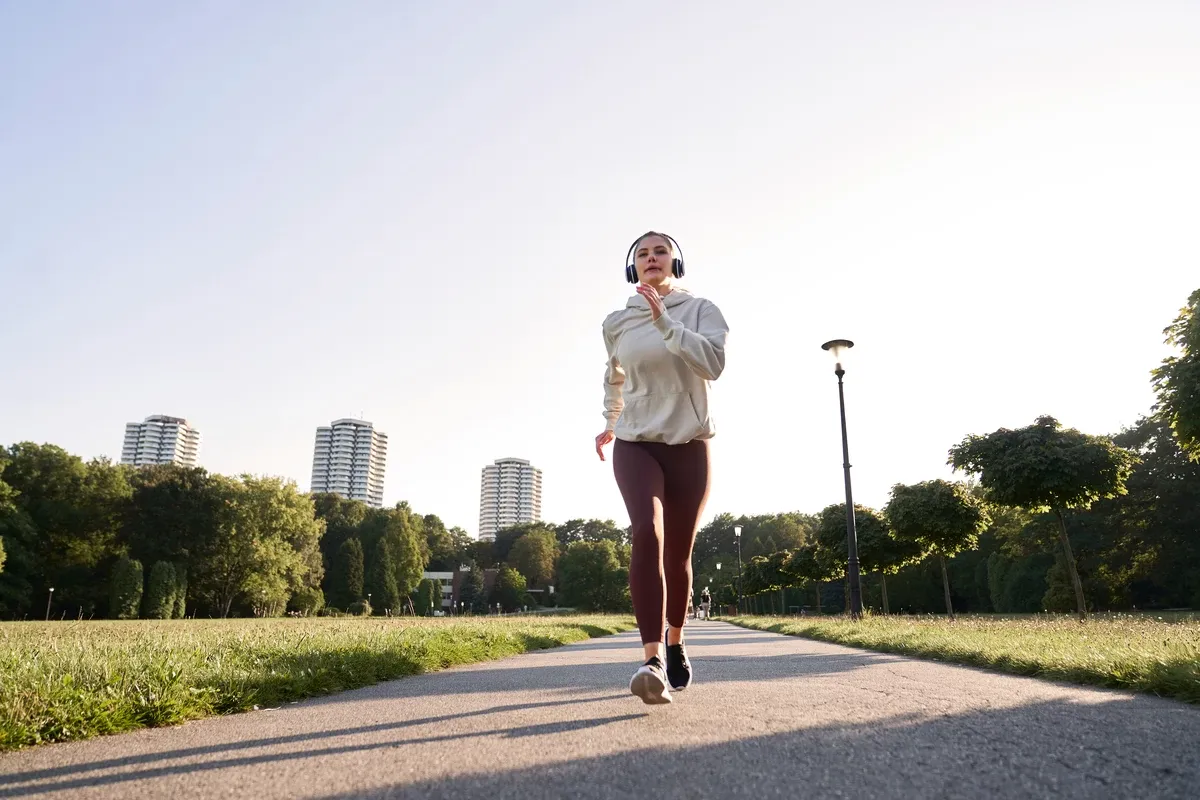 Mujer trotando al atardecer con audífonos deportivos
