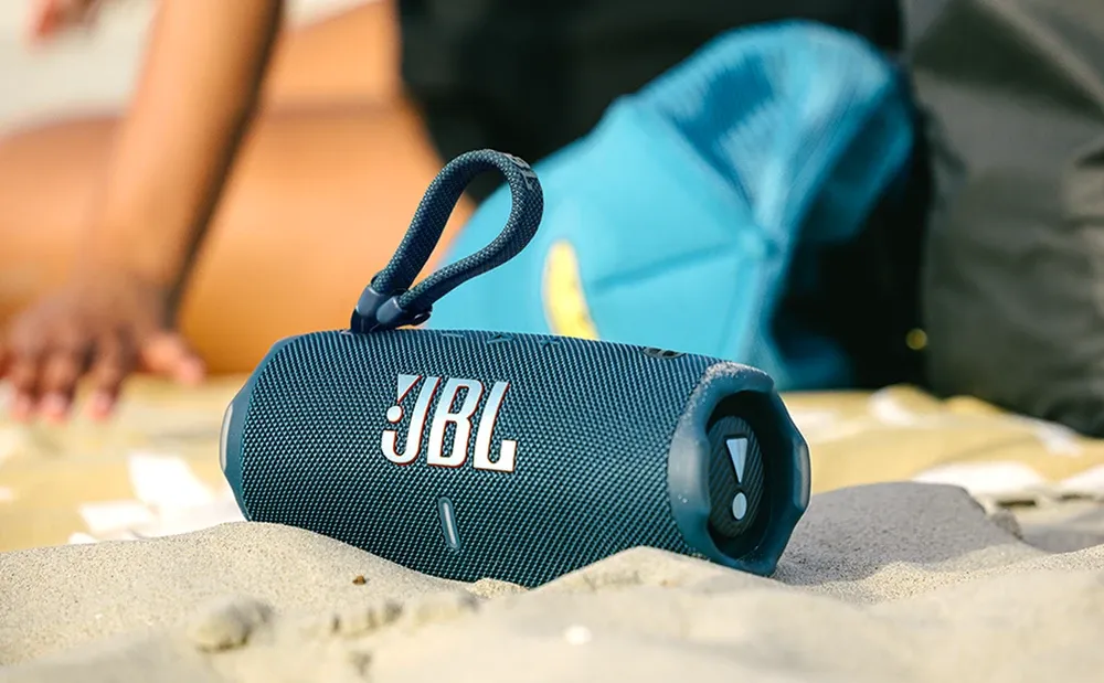 JBL Charge 6 colgado de su correa sobre la arena de la playa