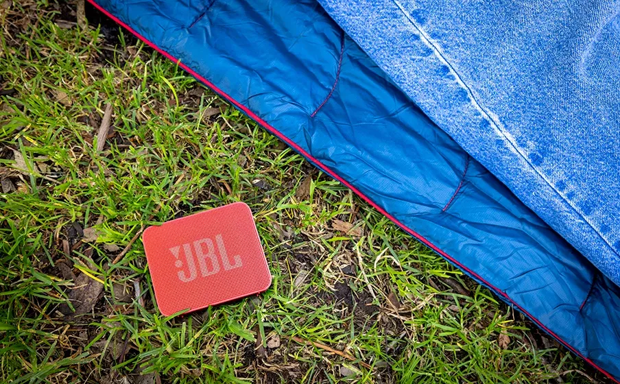 JBL Go Essential 2 rojo sobre el pasto junto a una manta