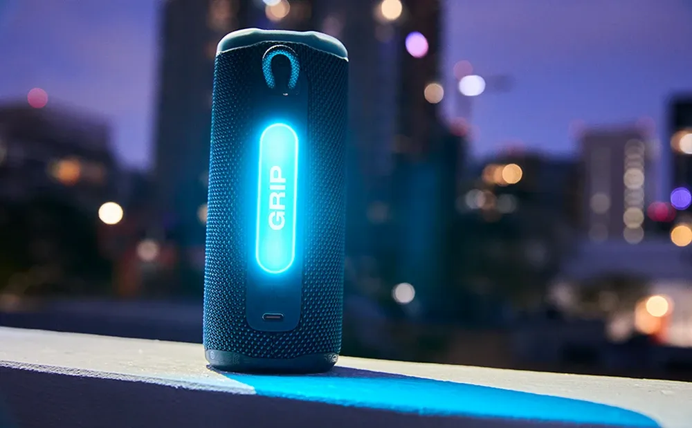 JBL Grip con la luz ambiental encendida de noche, con la ciudad de fondo