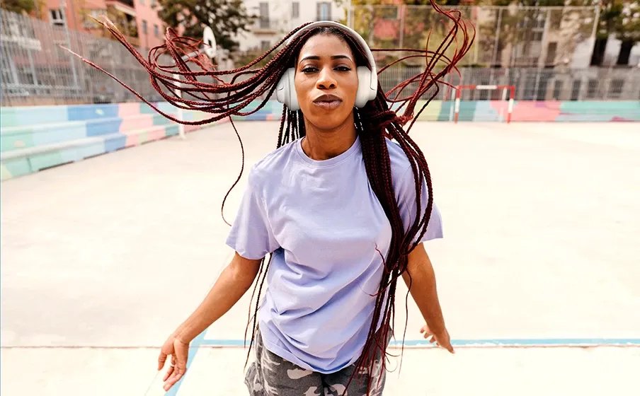 Mujer escuchando música con los JBL Tune 730BT blancos en una cancha